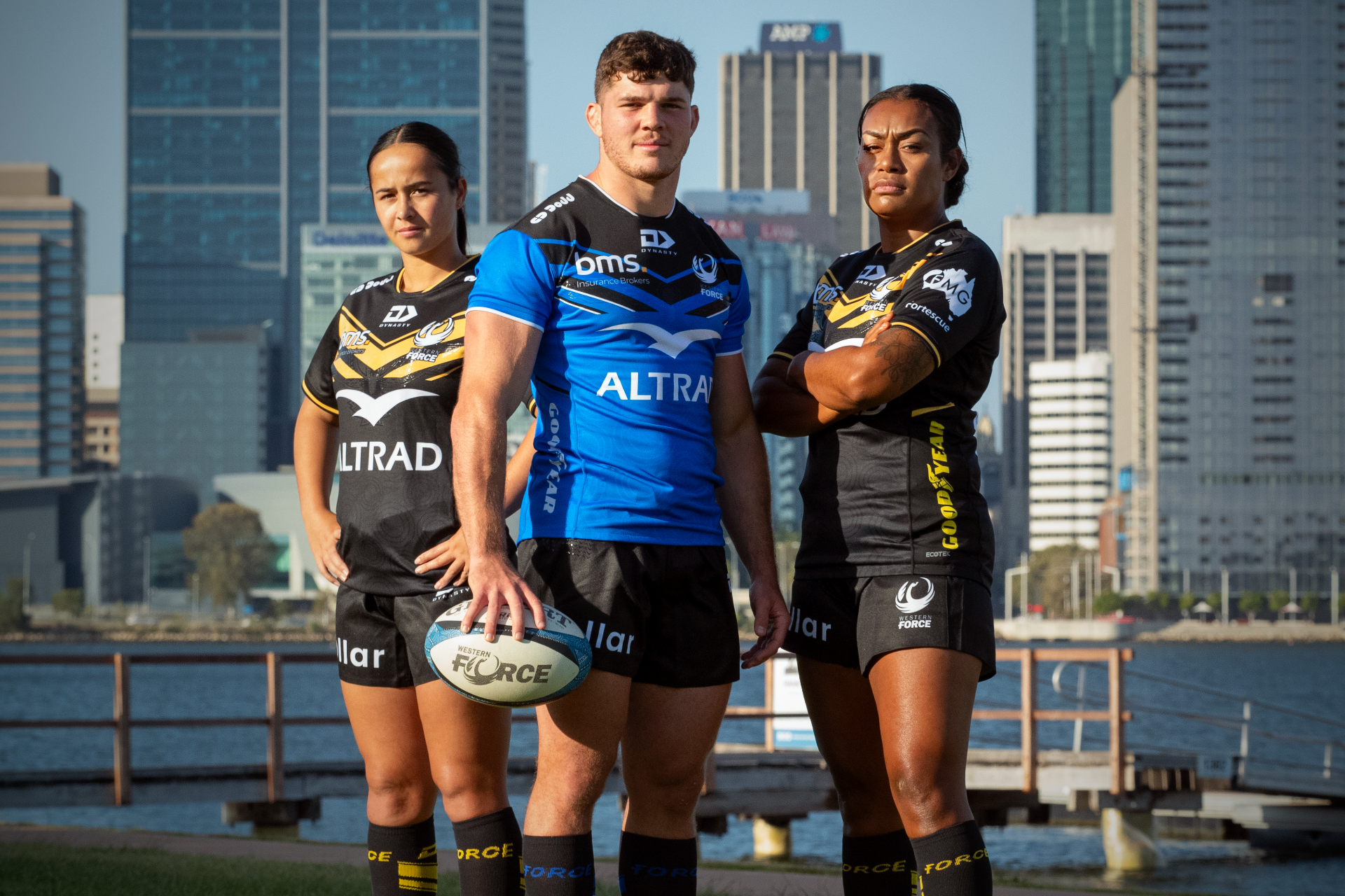 Nicole Ledington, Carlo Tizzano and Sara Ravatudei pose in the Western Force 2024 playing jerseys in front of the Swan River and Perth city skyline.